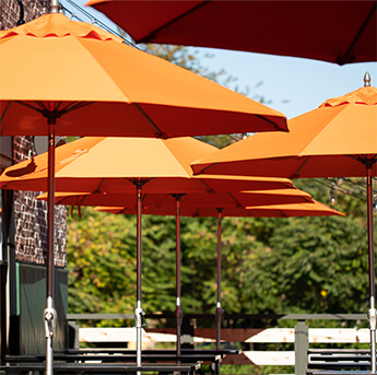 Close-up of a couple orange Frankford Monterey Umbrellas being used outside by a restaurant